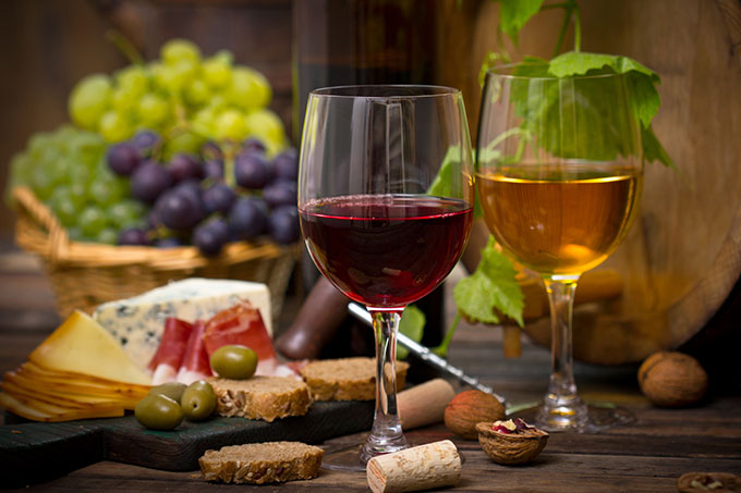 Glass of wine with grapes, cheese, cured meats, olives, and nuts.